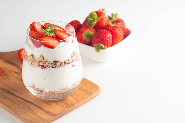 Glass with granola yogurt and fresh strawberries on white table Healthy breakfast bowl concept