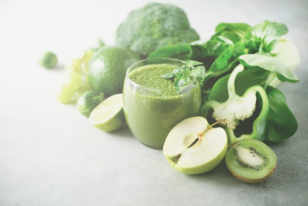 Glass with green health smoothie, kale leaves, lime, apple, kiwi, grapes, banana, avocado, lettuce.