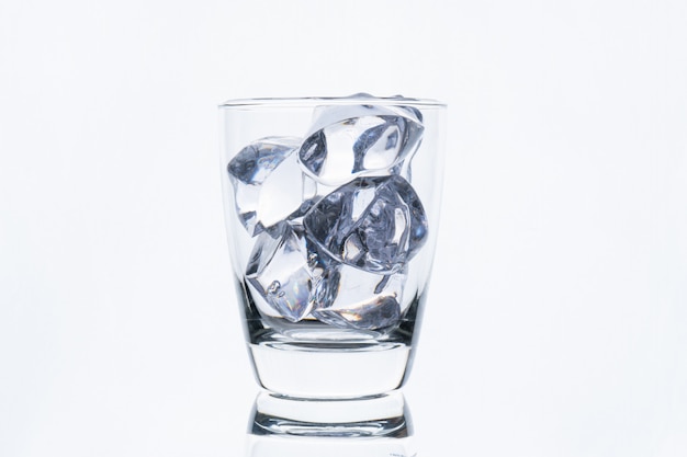 Glass with ice cube isolated on white wall