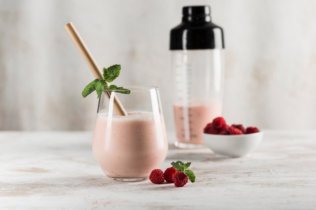 A glass with a Lassi drink with raspberries, mint, a bamboo tube and a cocktail shaker on a light background. Horizontal orientation. Side view. Indian traditional refreshing drink.