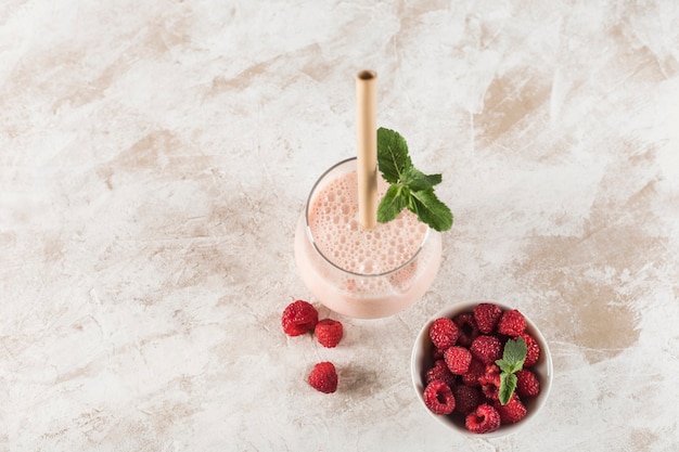 A glass with a Lassi drink with raspberries, mint and a bamboo tube on a light background. Horizontal orientation. Top view. Indian traditional refreshing drink.