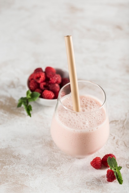 A glass with a Lassi drink with raspberries, mint and a bamboo tube on a light background. Vertical orientation. Top view. Indian traditional refreshing drink.