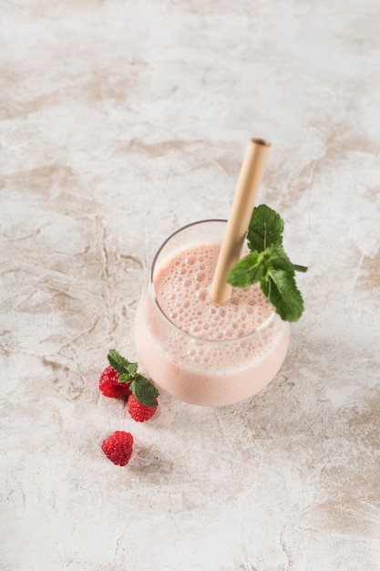 A glass with a Lassi drink with raspberries, mint and a bamboo tube on a light background. Vertical orientation. Top view. Indian traditional refreshing drink.