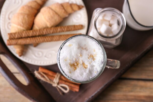 Glass with latte macchiato and tasty pastry on wooden tray