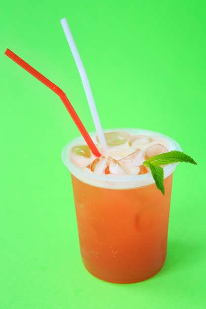 A glass with red lemonade with mint, cold refreshing drink or beverage with ice on green background