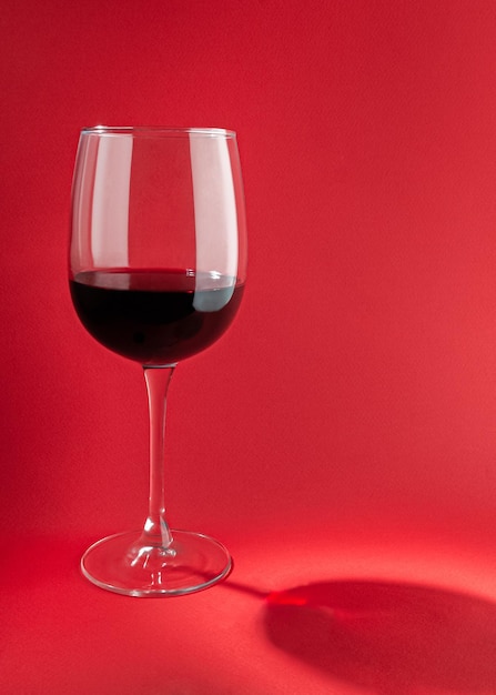 Glass with red wine On a plain red background Hard light sharp shadows Closeup Place for text