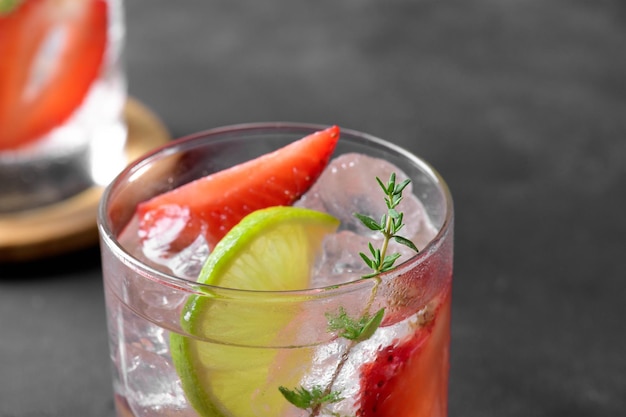 A glass with summer strawberry soda drink or mojito with strawberry ice cubes and lime on dark background