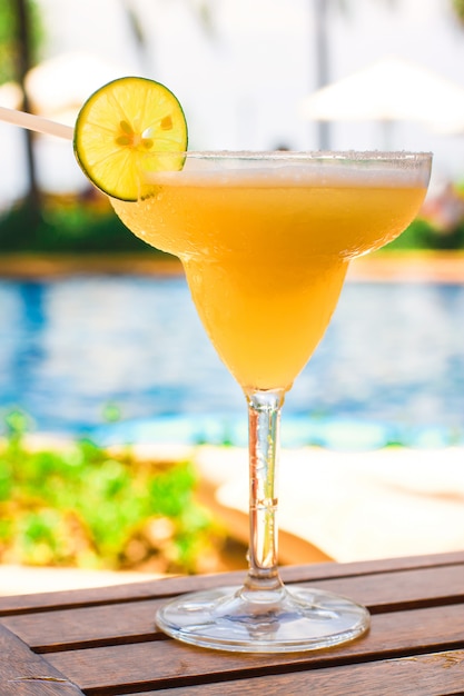 Glass with sweet alcoholic cocktail on wooden table in the exotic resort