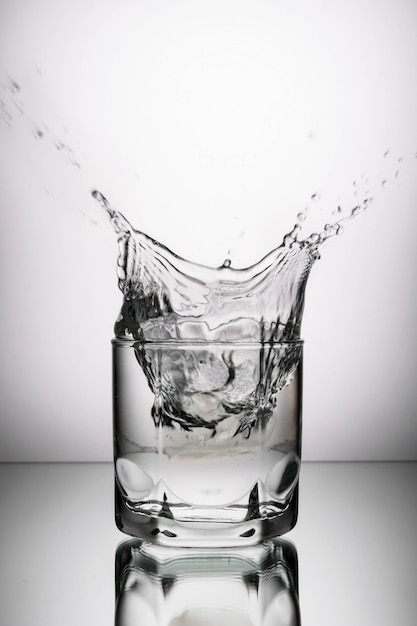 Glass with vodka, alcohol, water on a gray background with pieces of ice falling to it with splashes