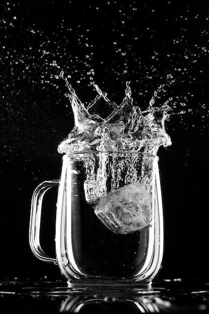 Glass with water ice and splashes on a black background