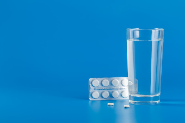 Glass with water and various pills isolated on blue background with copy space