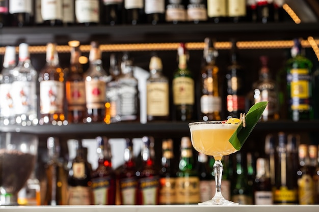 Glass with yellow lemon cocktail decorated with dried pineapple and mint on the blurred bar