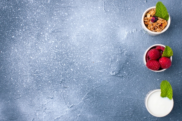 Photo a glass with yoghurt, muesli and berries on a gray background and a white plate