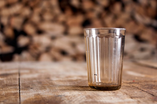 A glass on a wooden table and firewood behind