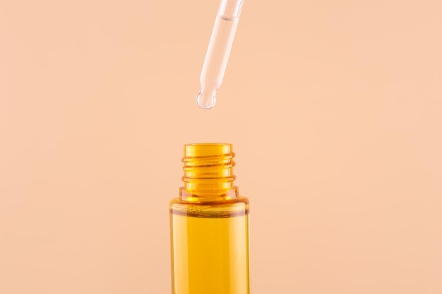 Glass yellow bottle with pipette with essential oil on beige background top view Aromatic cosmetic