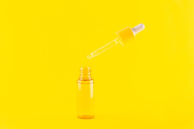 Glass yellow bottle with pipette with essential oil on yellow background top view Aromatic cosmetic