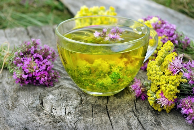 a glass of yellow flowers sits on a wooden table.