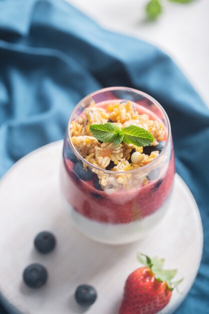 Glass of yogurt with strawberry mousse, blueberries and granola on a white background