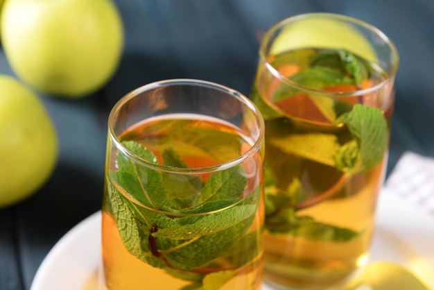 Glasses of apple juice with fruits and fresh mint on table close up