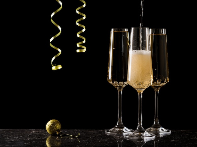 Glasses are filled with sparkling wine on a black background with a hanging serpentine.