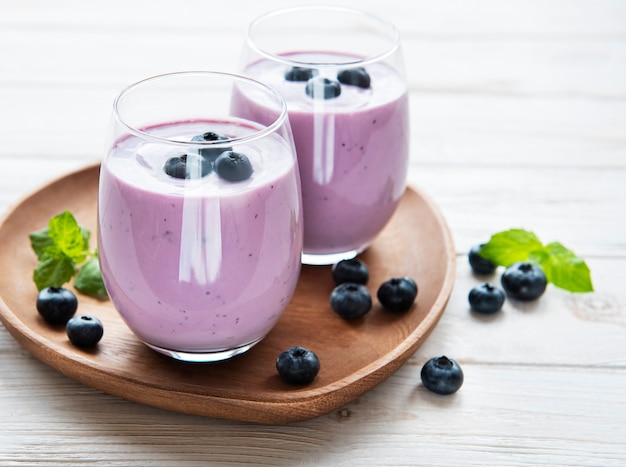 Glasses of blueberry yogurt with blueberries on a wooden background.