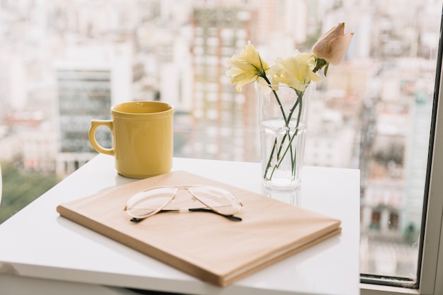 Glasses and book near flowers and mug on table