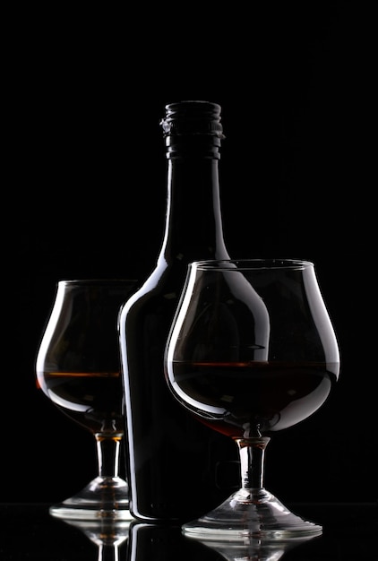 Glasses of brandy and bottle on black background