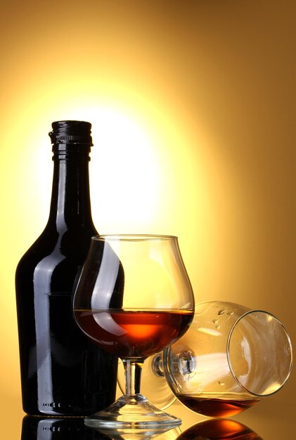 Glasses of brandy and bottle on yellow background