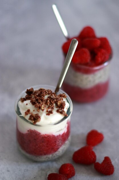 To glasses of chia pudding with yogurt and raspberry on grey marble table