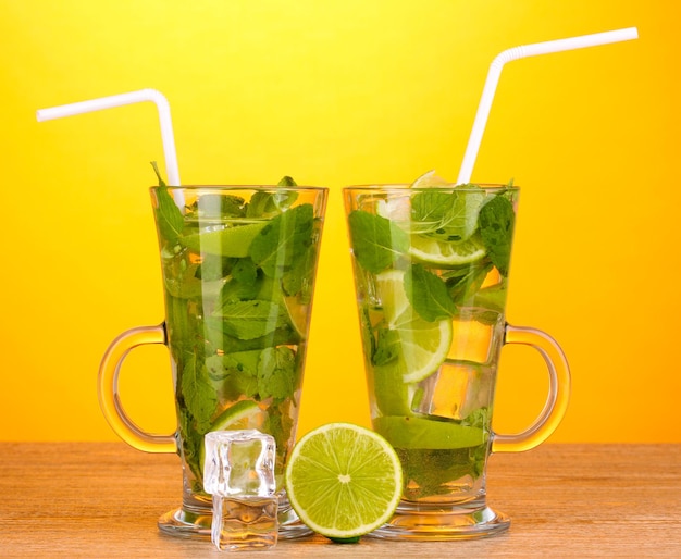 Glasses of cocktail with lime and mint on wooden table on yellow background