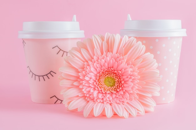 Glasses of coffee take-away and gerbera flower on pink pastel background. 