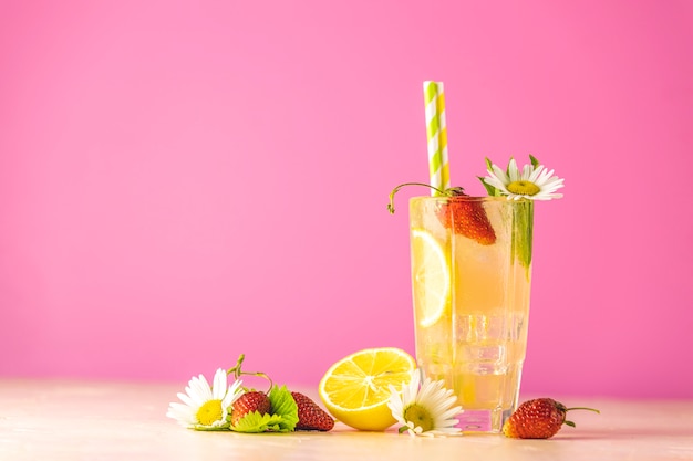 Glasses of cold icy refreshing drink with lemon and strawberry. Bright pink background