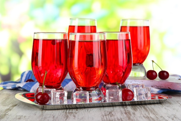 Glasses compote on board and metal tray on napkin on wooden table on nature background