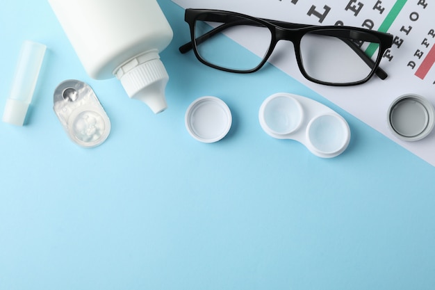 Glasses, contact lenses and eye test chart on blue surface, top view