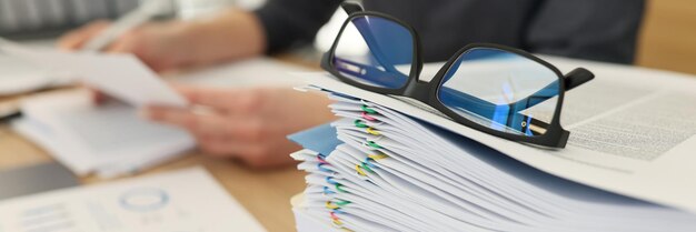 Glasses for eyesight lie on stack of documents at workplace in office woman studies