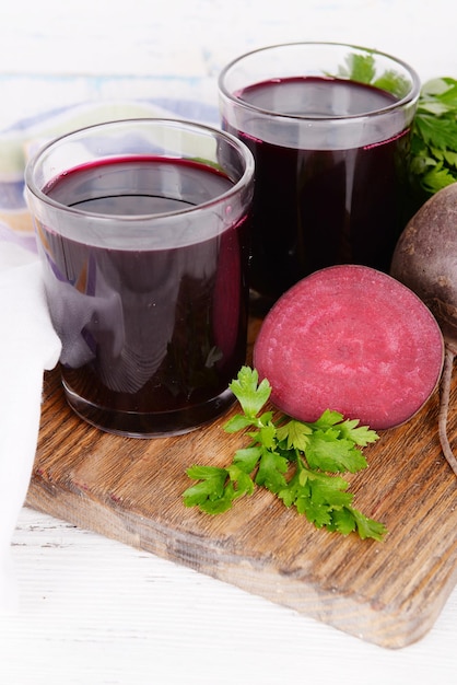 Glasses of fresh beet juice and vegetables on cutting board on wooden background