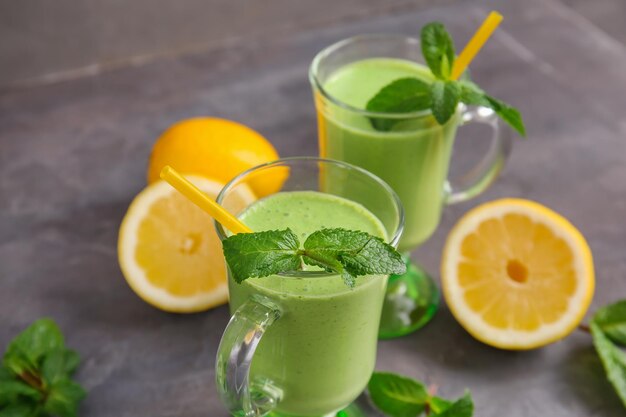 Glasses of green healthy juice with fruit and mint on table