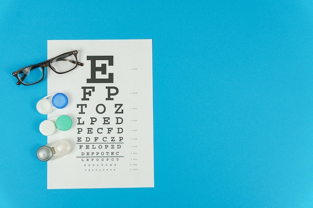 Glasses lens containers and a vision test table on the left on a blue background Copy space