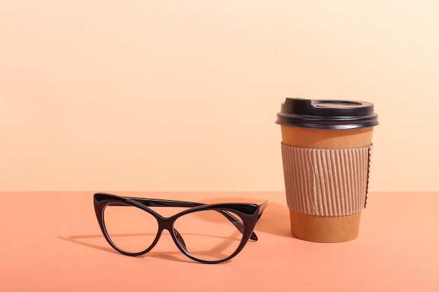 Glasses and a paper cup with coffee onn orange, morning is a tough shadow from the sun.