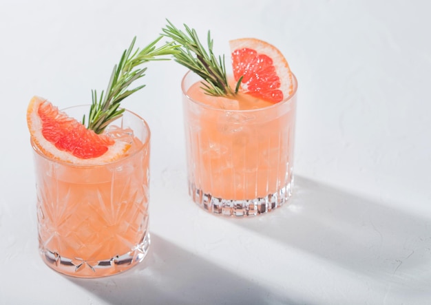 Glasses of refreshing summer red grapefruit cocktail with ice cubes fruit slice and rosemary on white background Space for text