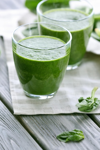 Glasses of spinach juice with napkin on wooden table closeup