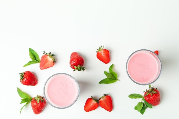 Glasses of strawberry milkshake and ingredients on white background