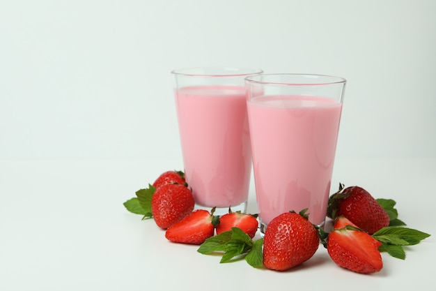 Glasses of strawberry milkshake and ingredients on white background