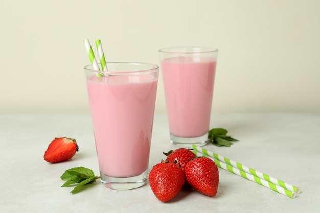 Glasses of strawberry milkshake and ingredients on white textured table