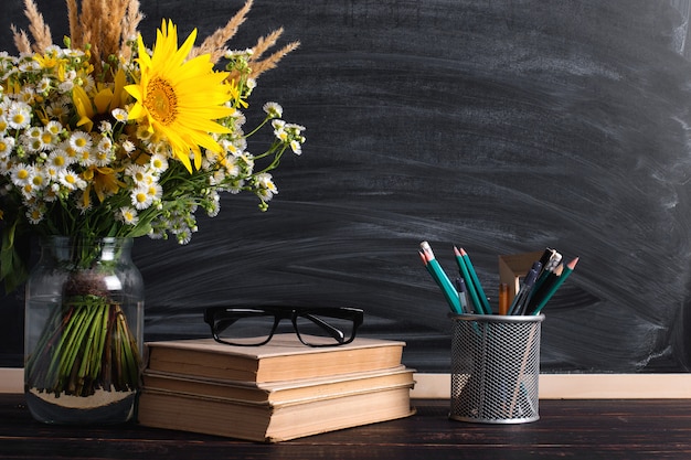 Photo glasses teacher books and wildflowers bouquet on the table, on blackboard with chalk.