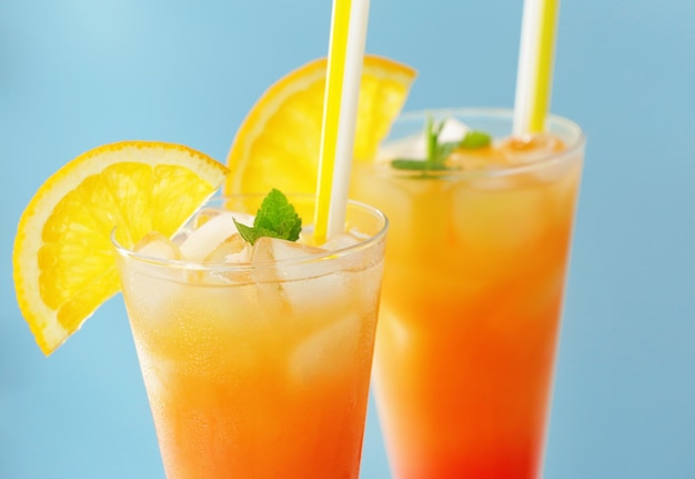 Glasses of Tequila Sunrise cocktail with orange slices on blue background closeup