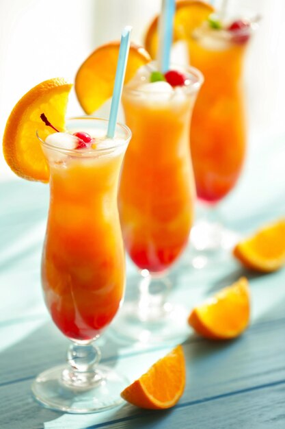 Glasses of Tequila Sunrise cocktail with orange slices on blue table