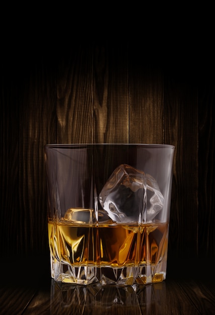 Glasses of whiskey with ice cubes on wood background