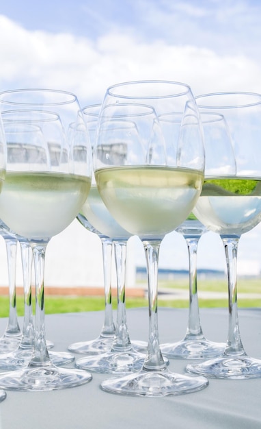 Glasses of white wine stand on a white tablecloth against a blue sky with clouds Vertical photo