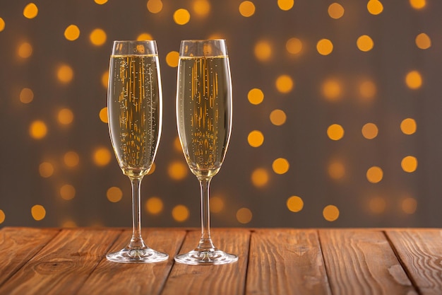 Glasses with champagne on a wooden background against a bokeh background of lights